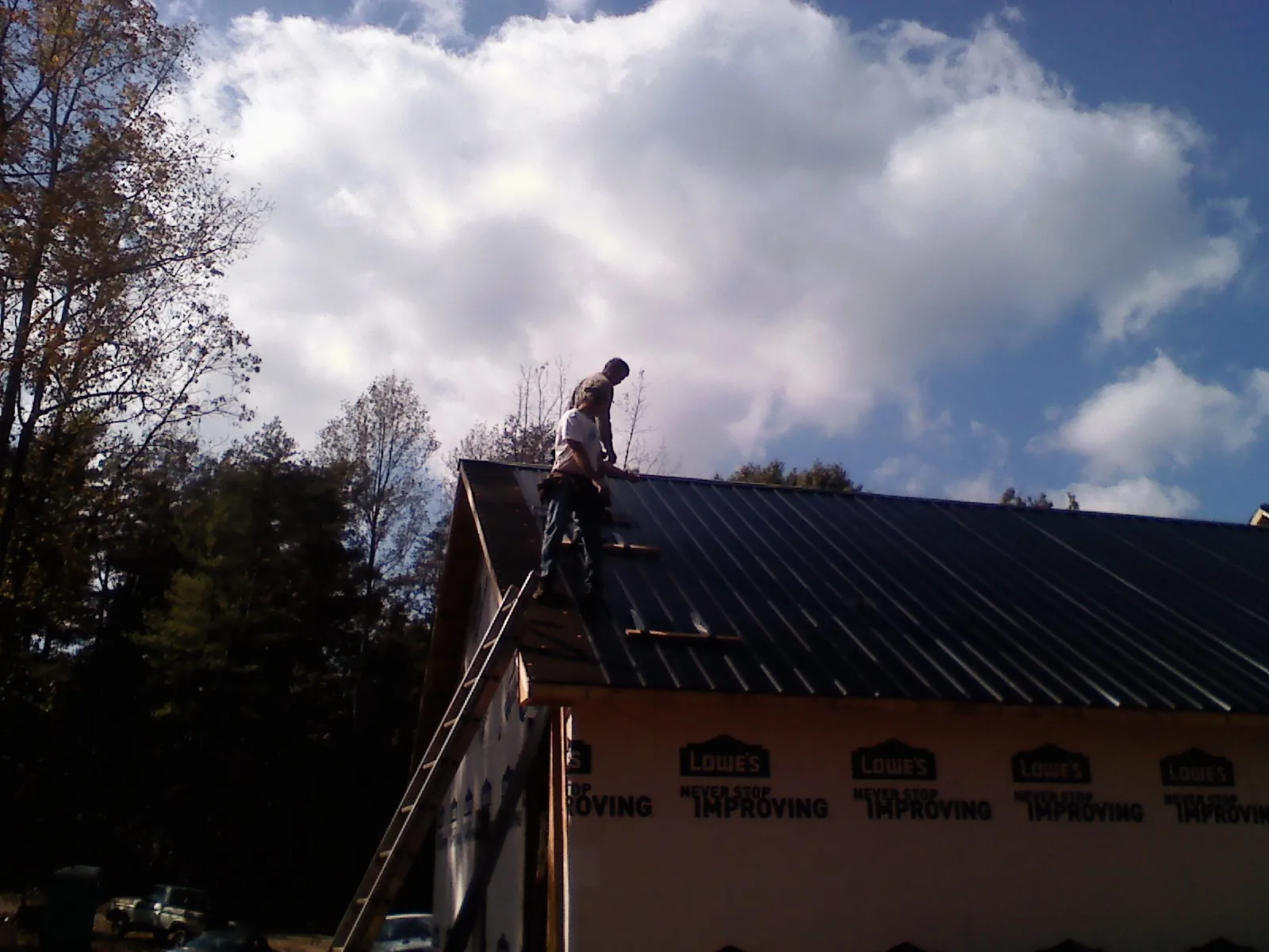Roofer fastening dark metal panels high against a cloudy sky, from a Roof Inspection job in Shelby